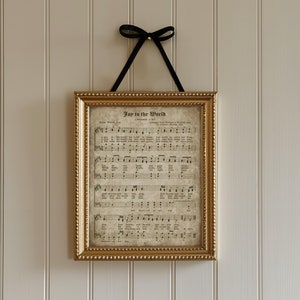 May include: A gold-framed print of the song "Joy to the World" with sheet music and lyrics. The print is hanging on a light beige wall with vertical wood paneling.