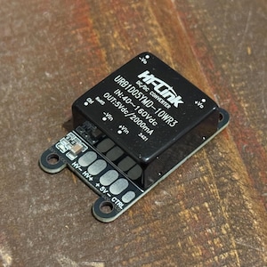 May include: A black DC/DC converter module with the text "Hi-Link URB1D05YMD-10WR3 DC/DC CONVERTER IN:40~160Vdc OUT:5Vdc/2000mA 2421" printed on the top. The module has several terminals labeled "HV-", "HV+", "+5V", and "CTRL".