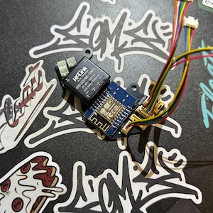 May include: A blue circuit board with a black module labeled "Hi-Link URB1005YMO-10WR3 IN: 40-160Vdc OUT: 5Vdc/2000mA". The board has a small blue chip labeled "Wi-Fi" and "FCC".