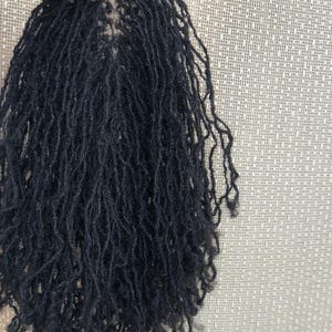 Könnte beinhalten: Ein Haarteil mit zahlreichen dünnen, schwarzen, texturierten Locs, die an einer beigen, netzartigen Basis befestigt sind. Die Locs sind lang, schmal und haben ein natürliches, leicht krauses Aussehen, das in einer dichten Schichtung herabhängt.
