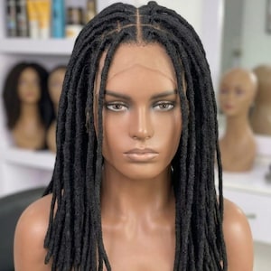May include: A shoulder-length black wig featuring textured faux locs with a center part. The wig is displayed on a mannequin head and includes a sheer lace front section that mimics a natural hairline along the forehead and temples.