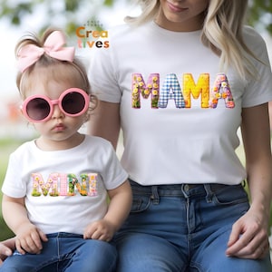 May include: A white t-shirt with the word "MAMA" in colorful patchwork letters. A matching white t-shirt with the word "MINI" in colorful patchwork letters is worn by a young child.