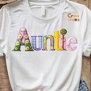 Puede incluir: Camiseta blanca con la palabra "Tía" escrita en letras de patchwork de colores. Las letras están decoradas con flores, vichy y un pequeño árbol.