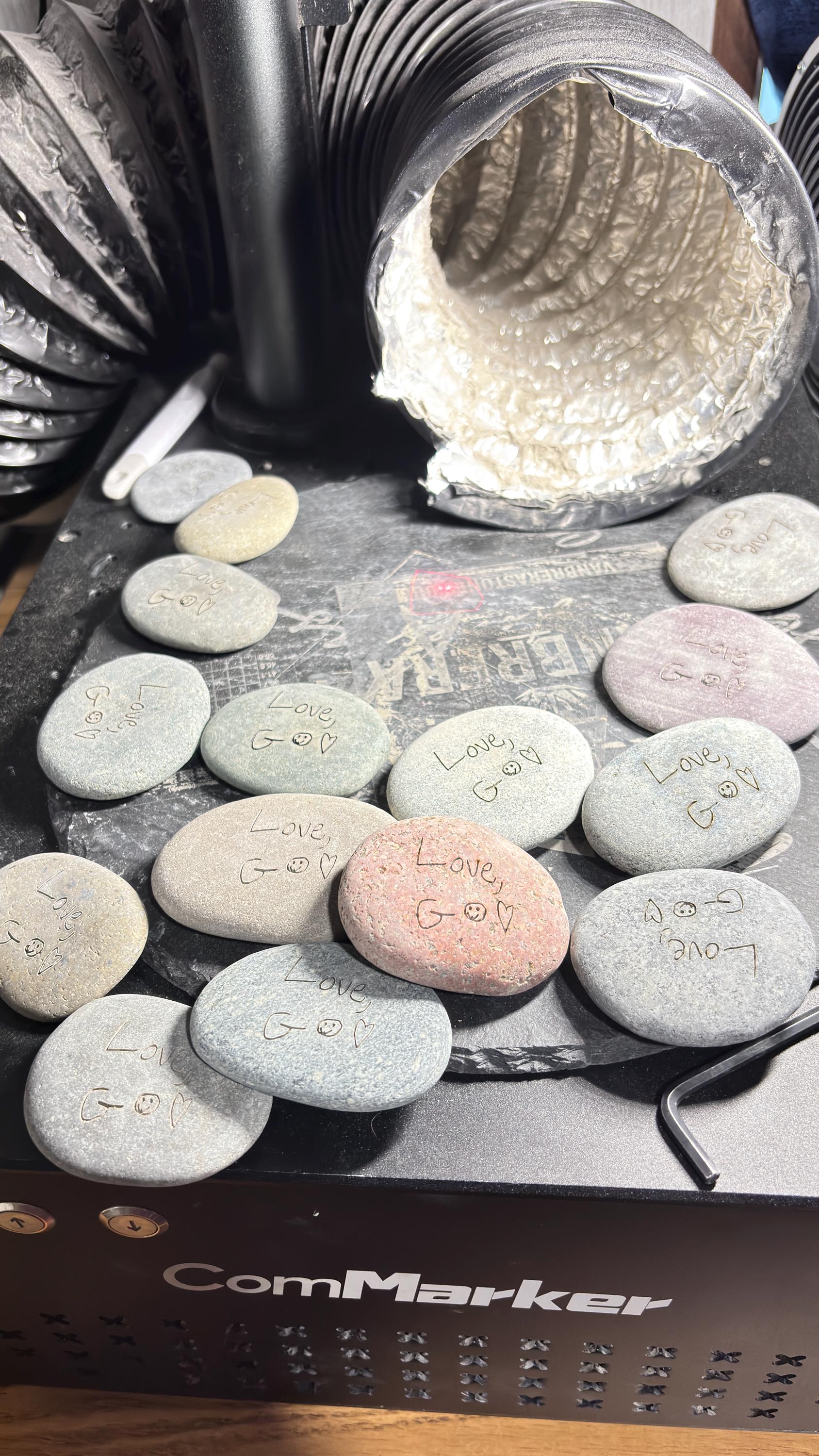 A collection of small, personalized river stones with various engravings like "Love,", smiley faces, and hearts.
