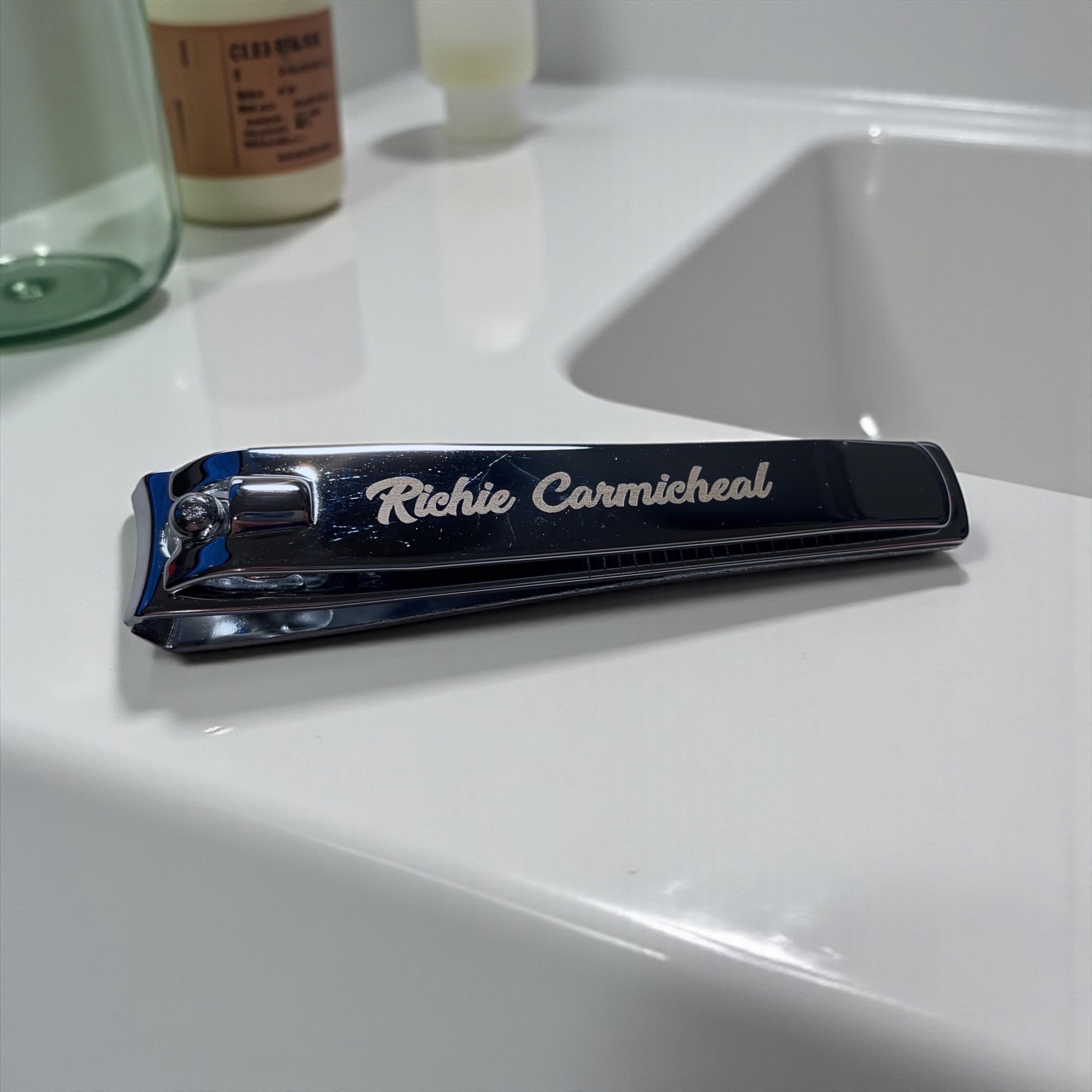 Personalized chrome nail clipper engraved with 'Richie Carmicheal' rests by a sink.
