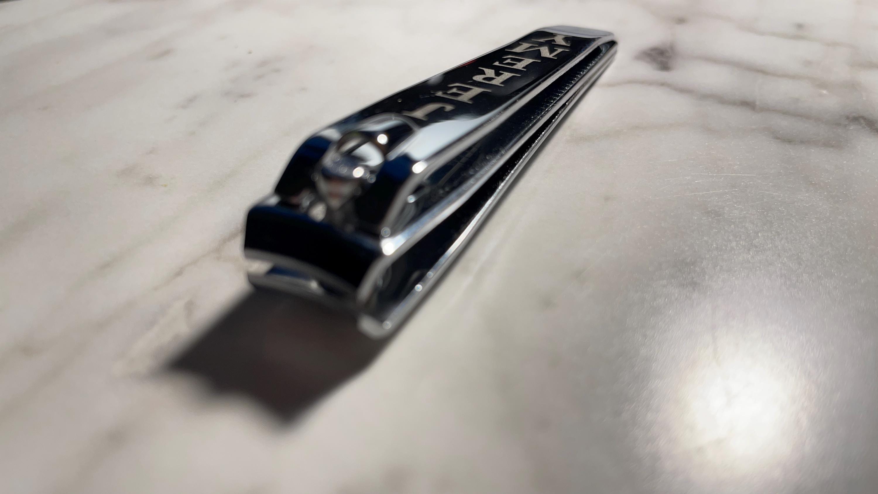 A close-up of a chrome stainless steel nail clipper resting on a white marbled surface.