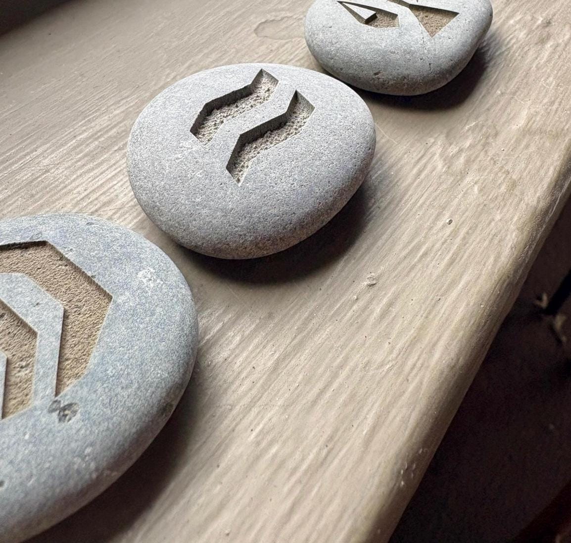 Three grey stones with geometric symbols engraved into them, placed on a textured surface.