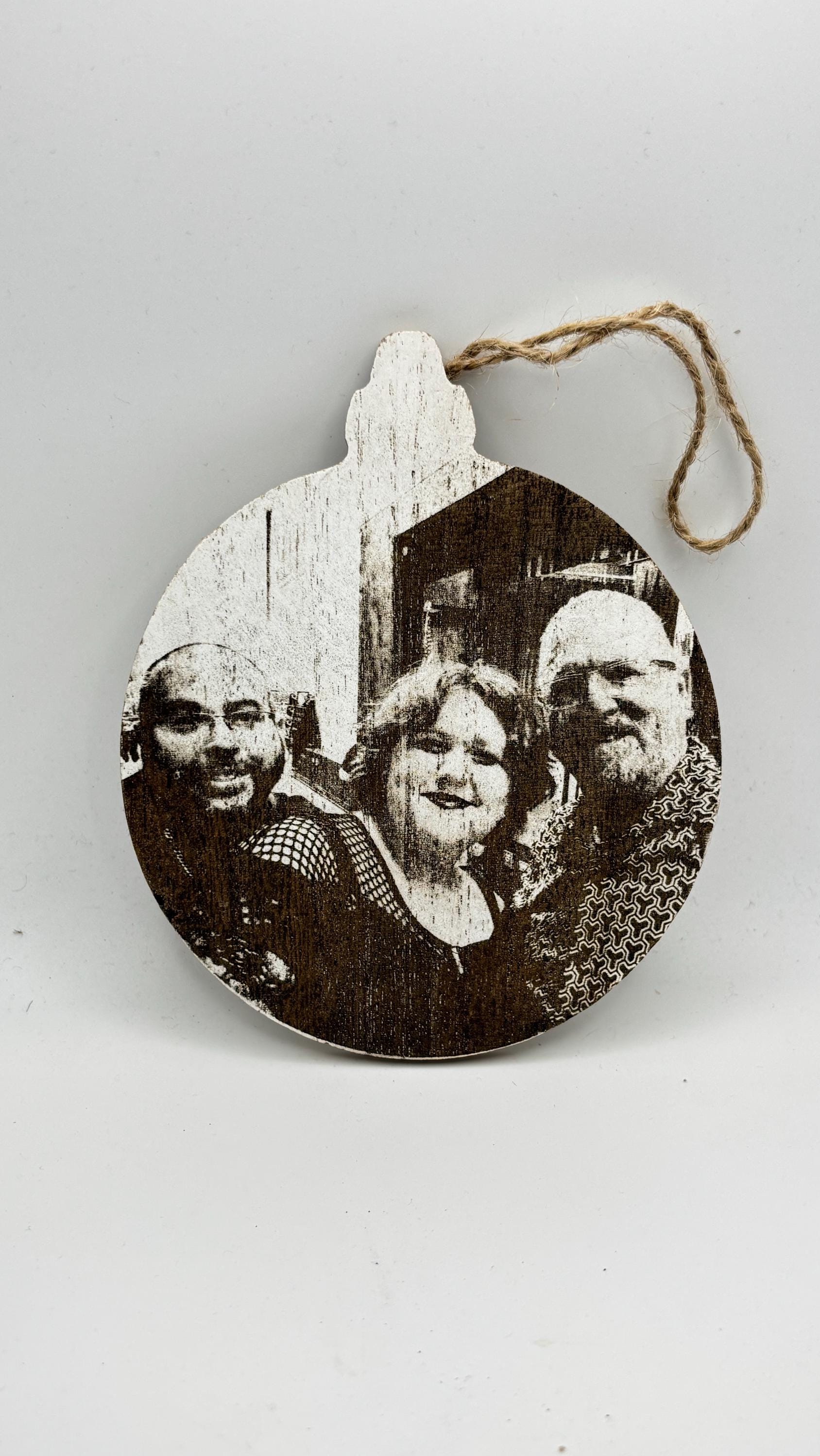 A round MDF ornament featuring an engraved portrait of three people with a natural twine hanging loop.