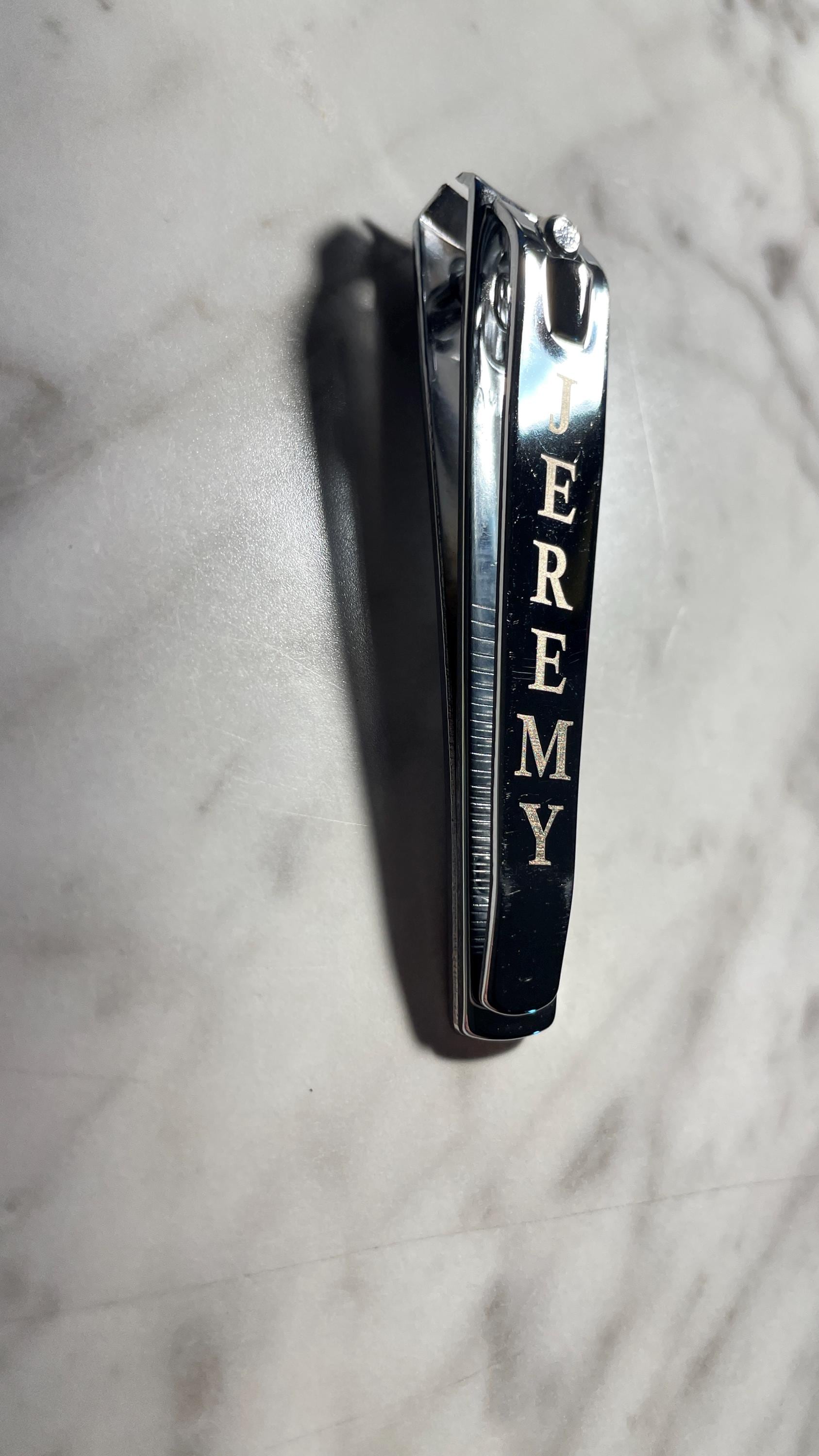 Side view of engraved chrome nail clippers with the name 'JEREMY' on marble.