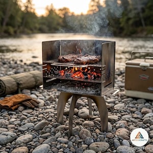 May include: A portable stainless steel charcoal grill with a three-legged base, featuring a rectangular firebox with side vents, a middle grate holding glowing hot coals, and a top cooking grate with two seared steaks cooking over the fire.