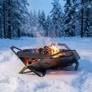 May include: A metal fire pit with a grill, burning wood, and flames. The fire pit is set in the snow with a forest background. The fire pit has a geometric design with cut-out shapes.