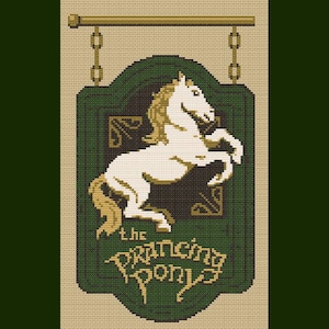 Op de afbeelding: Een kruissteekbord met een wit paard dat zich opricht tegen een donkergroene achtergrond. Het bord leest "The Prancing Pony" in een gestileerd lettertype, met een goudkleurige balk en kettingen aan de bovenkant.
