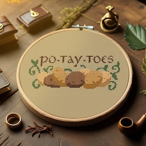 May include: A cross-stitch embroidery hoop with the word "PO-TAY-TOES" and potato illustrations. The image includes leather-bound books, a pipe, a ring, and other decorative items on a wooden surface.