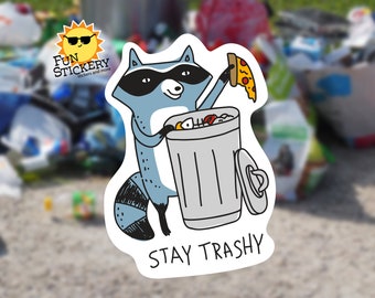 May include: A cartoon raccoon wearing a black eye mask is holding a slice of pizza and throwing it into a gray trash can. The trash can is full of other food scraps. The text "STAY TRASHY" is written below the raccoon and trash can.
