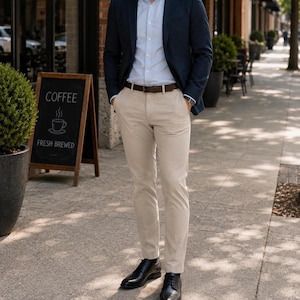 May include: A navy blue blazer, light blue button-down shirt, and khaki pants. The outfit is paired with a brown belt and black dress shoes. A sign in the background reads "COFFEE FRESH BREWED".