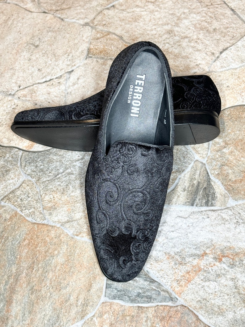 Puede incluir: Zapatos negros de terciopelo sin cordones con un intrincado estampado floral. Los zapatos tienen una puntera redondeada y un tac&oacute;n bajo. La marca "TERRONI DESIGN" es visible en la plantilla. Talla 43.