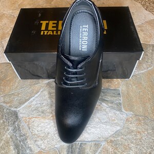 May include: Black leather dress shoe with laces, displayed on top of a black box. The shoe has a rounded toe and a low heel. The box has the words "TERRONI ITALIAN DESIGN" printed on it.