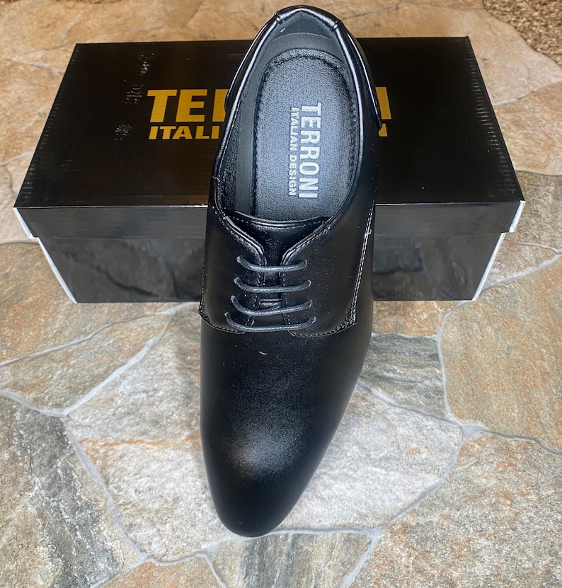 May include: Black leather dress shoe with laces, displayed on top of a black box. The shoe has a rounded toe and a low heel. The box has the words "TERRONI ITALIAN DESIGN" printed on it.