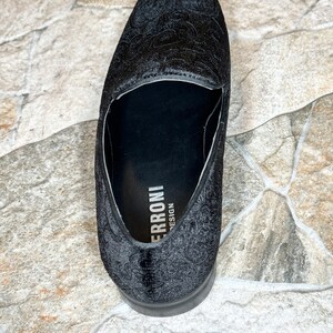 Puede incluir: Mocas&iacute;n negro de terciopelo con un estampado floral en relieve. El zapato tiene una puntera redondeada y un tac&oacute;n bajo. La marca "ERRONI DESIGN" es visible en la plantilla. Adecuado para ocasiones formales.