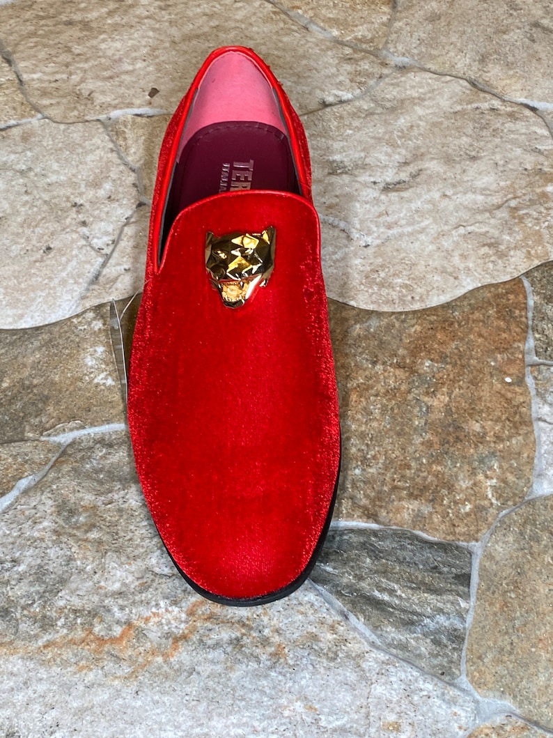 May include: A red velvet loafer with a gold-colored panther head emblem. The shoe has a rounded toe and a black sole. The interior is pink and burgundy. The shoe is a size 10.