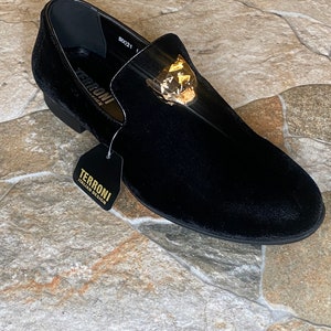May include: Black velvet loafer with a gold-coloured decorative accent. The shoe has a low heel and a tag that reads "TERRONI ITALIAN DESIGN". The shoe is a size 50021.
