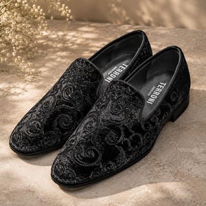 Puede incluir: Un par de mocasines negros de terciopelo con un intrincado dise&ntilde;o floral. Los zapatos tienen un dise&ntilde;o cl&aacute;sico sin cordones y un tac&oacute;n bajo. La marca "TERRONI DESIGN" es visible en el interior.