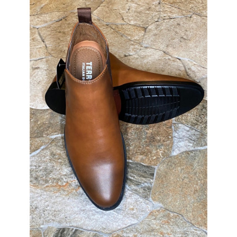 May include: A pair of brown leather Chelsea boots with a pointed toe and black rubber soles. The boots have a pull tab at the back and the brand name "TERRA ITALIAN DESIGN" is visible on the insole.