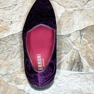 Op de afbeelding: Een enkele, dieppaarse fluwelen loafer met een sierlijk bloemmotief. De schoen heeft een ronde neus en een zwarte zool. De binnenkant is diep magenta, met de merknaam "ERRONI DESIGN" in het wit gedrukt.