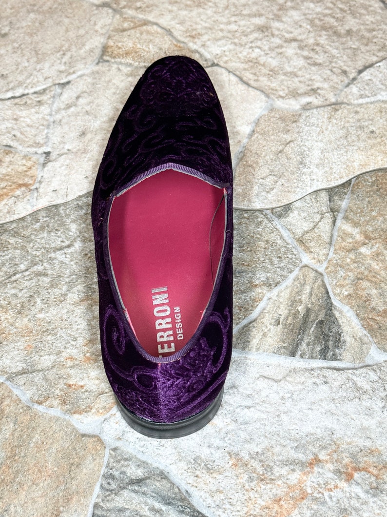 Op de afbeelding: Een enkele, dieppaarse fluwelen loafer met een sierlijk bloemmotief. De schoen heeft een ronde neus en een zwarte zool. De binnenkant is diep magenta, met de merknaam "ERRONI DESIGN" in het wit gedrukt.