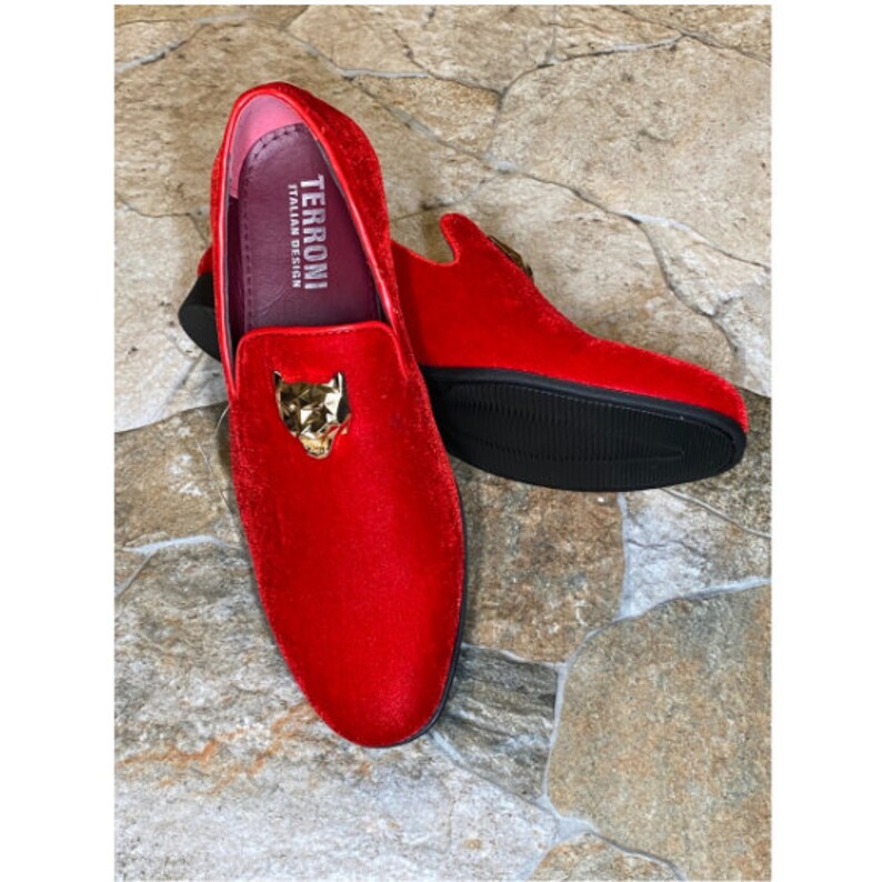 May include: A pair of red velvet loafers with a gold-colored panther head emblem on the vamp. The shoes have a black sole and the interior is pink. The brand name "TERRONI ITALIAN DESIGN" is visible inside the shoe.