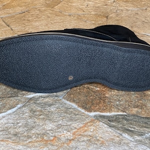 May include: Black suede shoe with a textured rubber sole. The shoe has a low profile and a gold-colored trim. The sole is marked with the number 10. The shoe is designed for comfort and style.