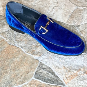Puede incluir: Un solo mocas&iacute;n de terciopelo azul real con un detalle met&aacute;lico dorado. El zapato tiene una punta redondeada y un tac&oacute;n bajo. La marca "TERRONI DESIGN" es visible dentro del zapato.