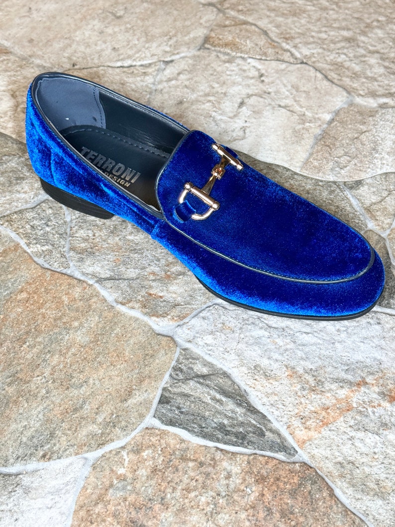Puede incluir: Un solo mocas&iacute;n de terciopelo azul real con un detalle met&aacute;lico dorado. El zapato tiene una punta redondeada y un tac&oacute;n bajo. La marca "TERRONI DESIGN" es visible dentro del zapato.