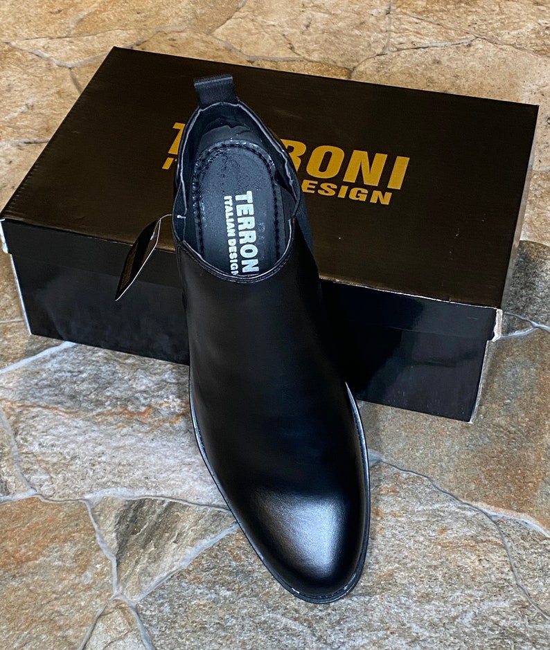 Puede incluir: Bota Chelsea de cuero negro con punta afilada, frente a una caja negra. La caja tiene letras doradas que dicen "TERRONI DESIGN". La plantilla de la bota dice "TERRONI ITALIAN DESIGN".