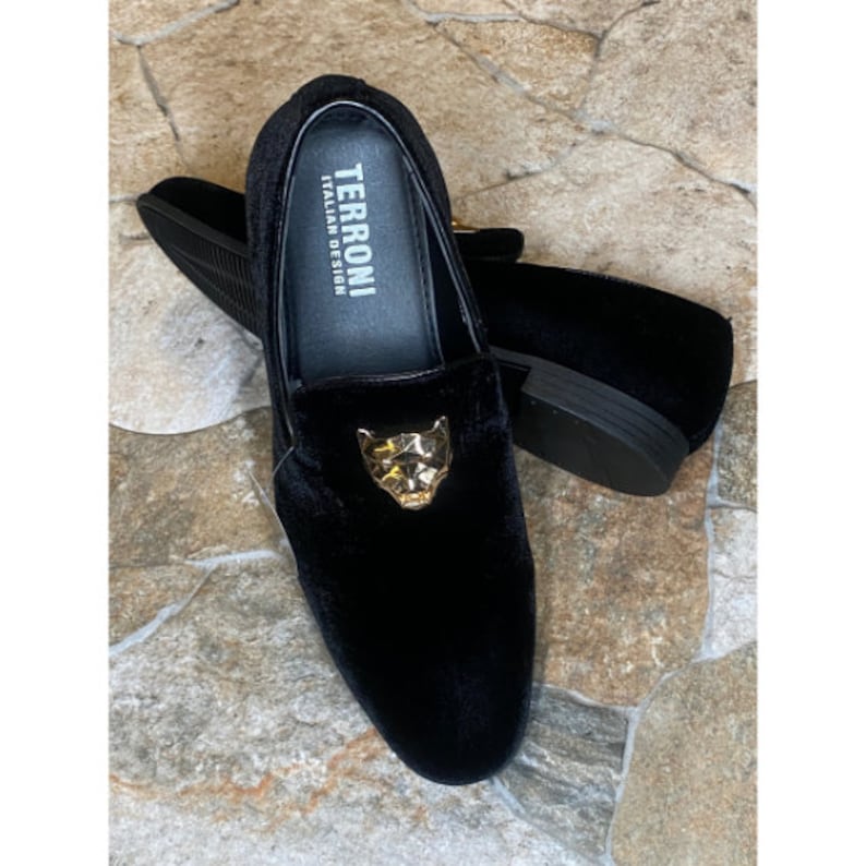 May include: Black velvet loafers with a gold panther head emblem. The shoes have a classic slip-on design and a low heel. The brand name "TERRONI ITALIAN DESIGN" is visible on the insole.