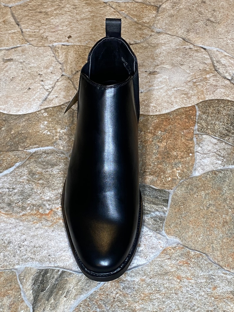 Puede incluir: Una bota Chelsea de cuero negro. La bota tiene una puntera redondeada, paneles laterales el&aacute;sticos y una leng&uuml;eta en la parte trasera. El cuero tiene un acabado pulido. La bota est&aacute; dise&ntilde;ada para el uso diario.