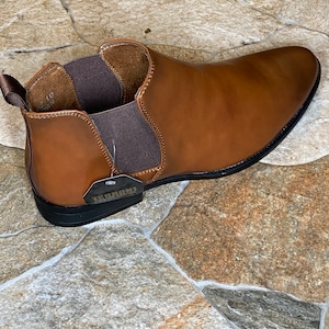 May include: A brown leather Chelsea boot with a black sole. The boot has elastic side panels and a pull tab at the back. A tag with the brand name "TERRONI" is attached. The shoe size is 10.