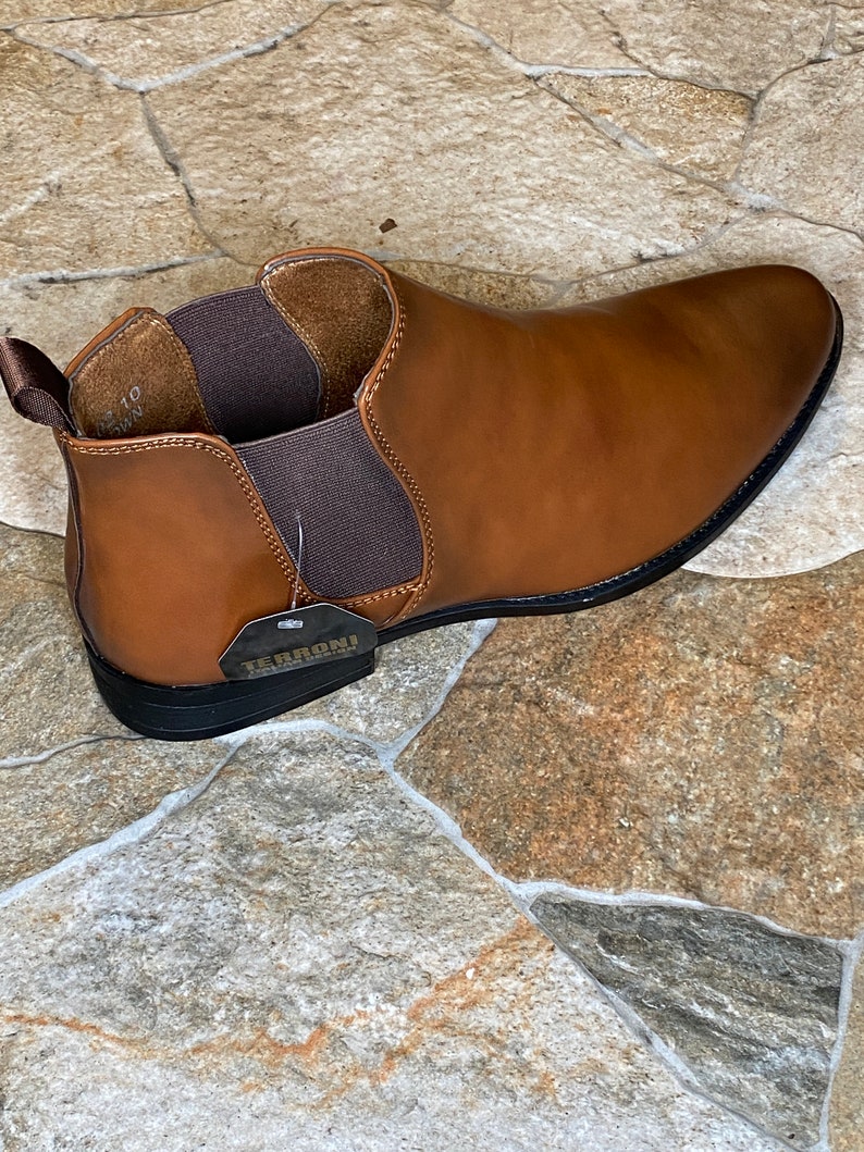 May include: A brown leather Chelsea boot with a black sole. The boot has elastic side panels and a pull tab at the back. A tag with the brand name "TERRONI" is attached. The shoe size is 10.