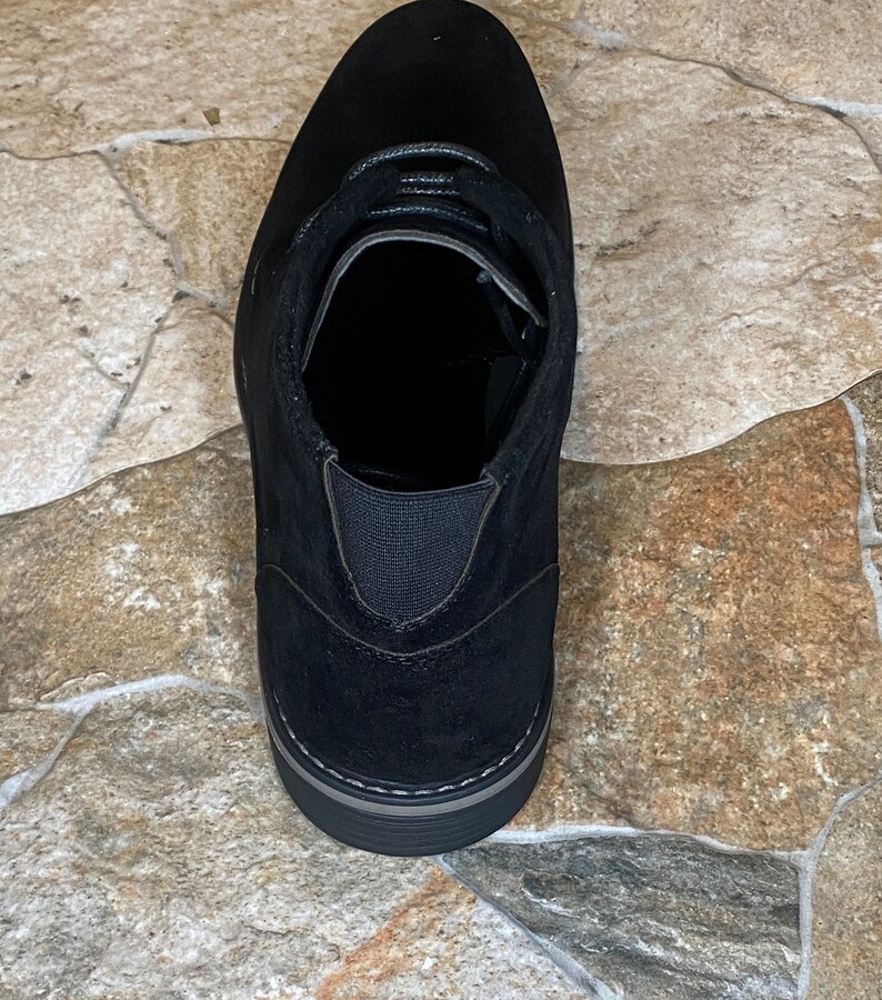May include: Black suede ankle boot with a rounded toe and a lace-up design. The boot features a gray sole and elastic side panels for easy wear. A versatile shoe for various occasions.
