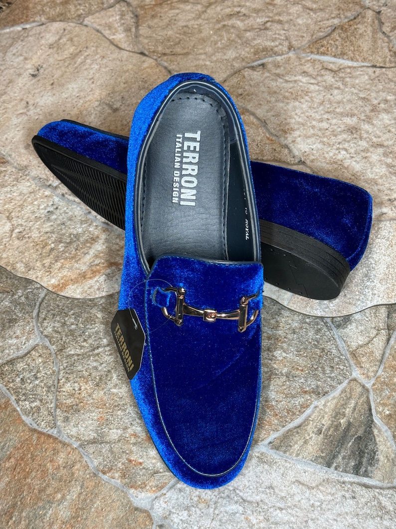 Puede incluir: Mocasines de terciopelo azul real con hebilla met&aacute;lica dorada. Los zapatos tienen suela negra y la marca "TERRONI ITALIAN DESIGN" es visible en la plantilla. Una etiqueta con el nombre de la marca est&aacute; adjunta.