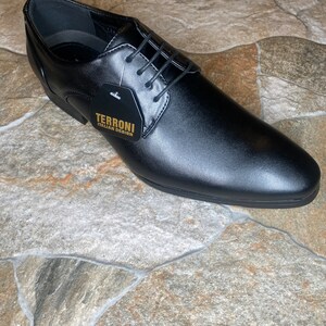 May include: A black leather dress shoe with a pointed toe and lace-up closure. The shoe has a tag that reads "TERRONI ITALIAN DESIGN". The shoe is displayed on a stone tile surface.
