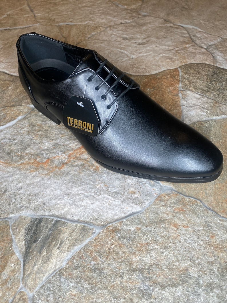 May include: A black leather dress shoe with a pointed toe and lace-up closure. The shoe has a tag that reads "TERRONI ITALIAN DESIGN". The shoe is displayed on a stone tile surface.