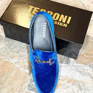 Puede incluir: Mocas&iacute;n de terciopelo azul con hebilla dorada, presentado con su caja negra. La caja tiene letras doradas que dicen "TERRONI ITALIAN DESIGN". El zapato tiene una plantilla de cuero con el nombre de la marca.