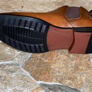 May include: A brown leather Chelsea boot with a black rubber sole. The sole has a textured pattern for grip. The boot's design includes a brown heel and a brown elastic side panel.