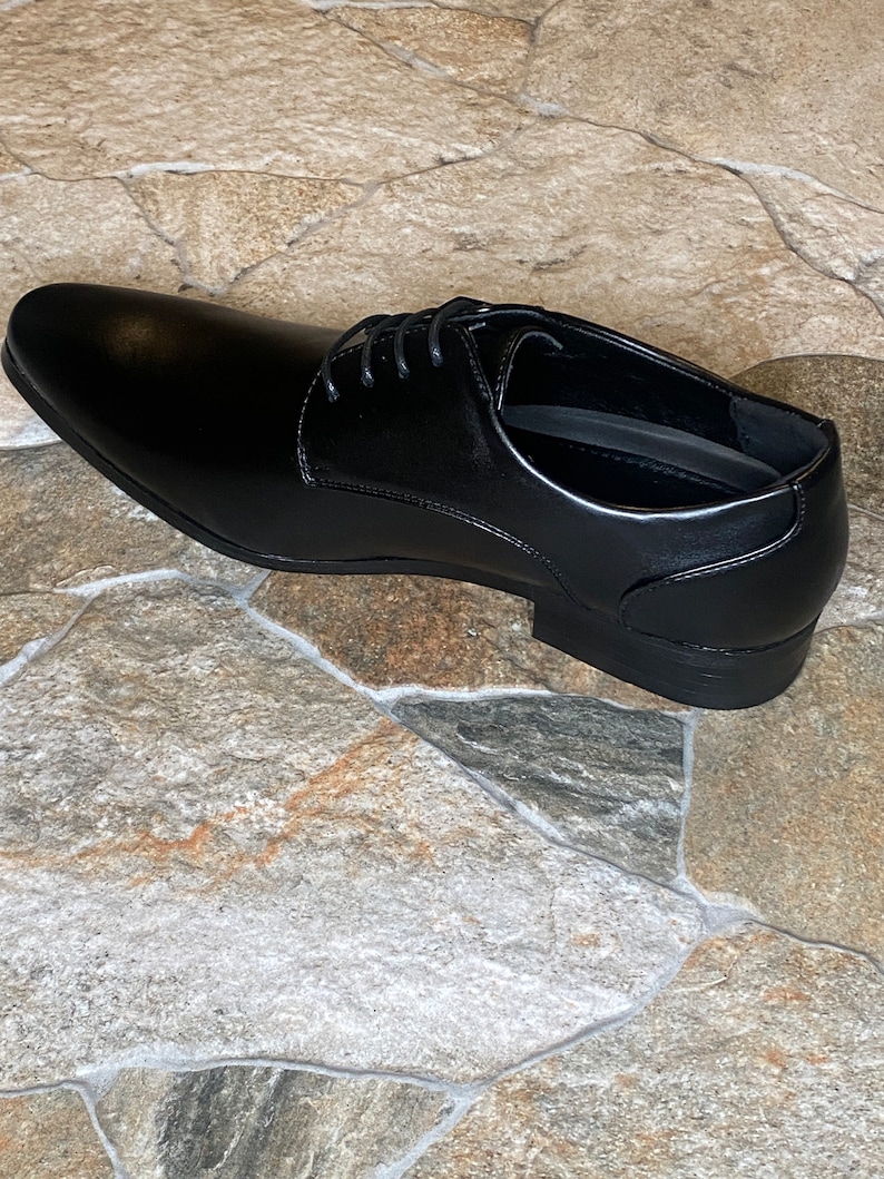 May include: A single black leather dress shoe with a pointed toe and lace-up closure. The shoe is displayed on a stone-like surface. The shoe is a classic style, suitable for formal occasions.
