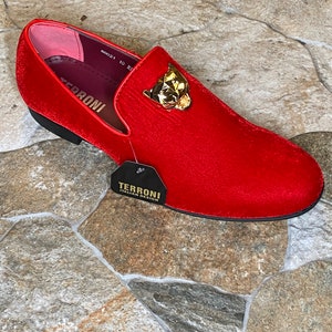 May include: A red velvet loafer with a gold-colored panther head ornament. The shoe has a black sole and a tag that reads "TERRONI ITALIAN DESIGN". The shoe size is 10.