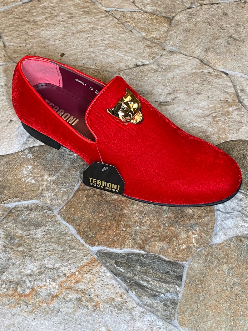 May include: A red velvet loafer with a gold-colored panther head ornament. The shoe has a black sole and a tag that reads "TERRONI ITALIAN DESIGN". The shoe size is 10.