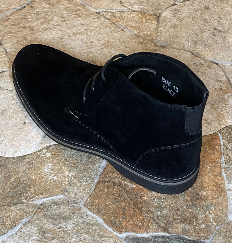 May include: Black suede chukka boot with a rounded toe and a gray sole. The boot has a lace-up closure and an elastic panel at the ankle. The text "B05 10 Black" is visible inside the boot.