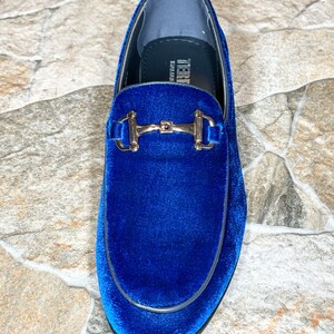 Puede incluir: Un solo mocas&iacute;n de terciopelo azul real con una hebilla dorada. El zapato tiene una puntera redondeada y un ribete negro. El interior es de color azul claro. La marca "TERRE" es visible dentro del zapato.