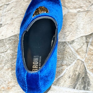 May include: A single, royal blue velvet loafer with a gold-colored geometric embellishment. The shoe has a black sole and trim. The brand name "BRROW" is visible on the insole. The shoe is a size 10.